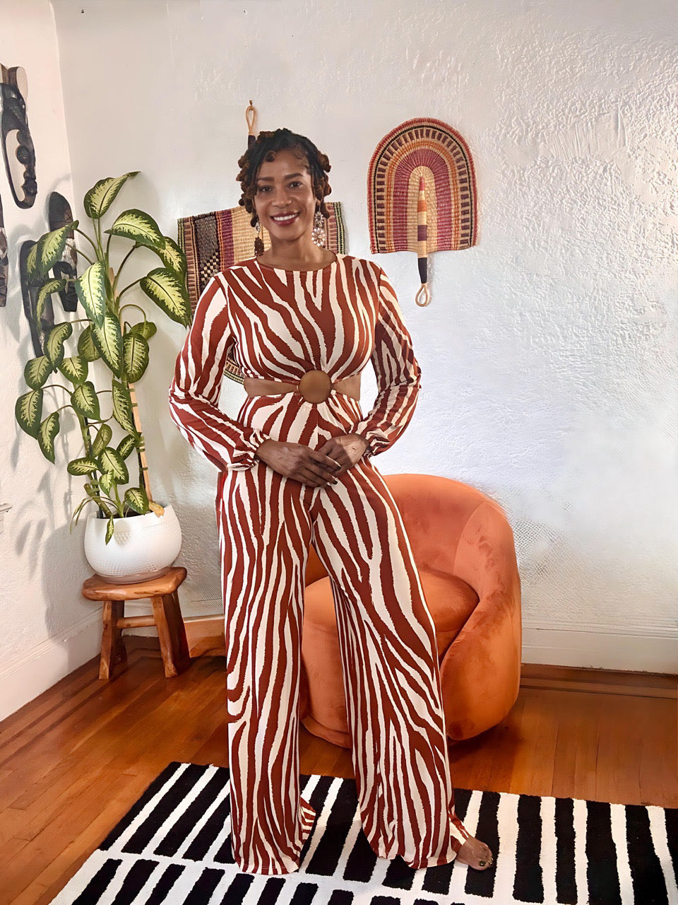 Model wearing the MAKE ME WILD Zebra Print Cut-Out Jumpsuit from MonologueClosets — brown and cream zebra stripes with circular cut-out waist and long sleeves.