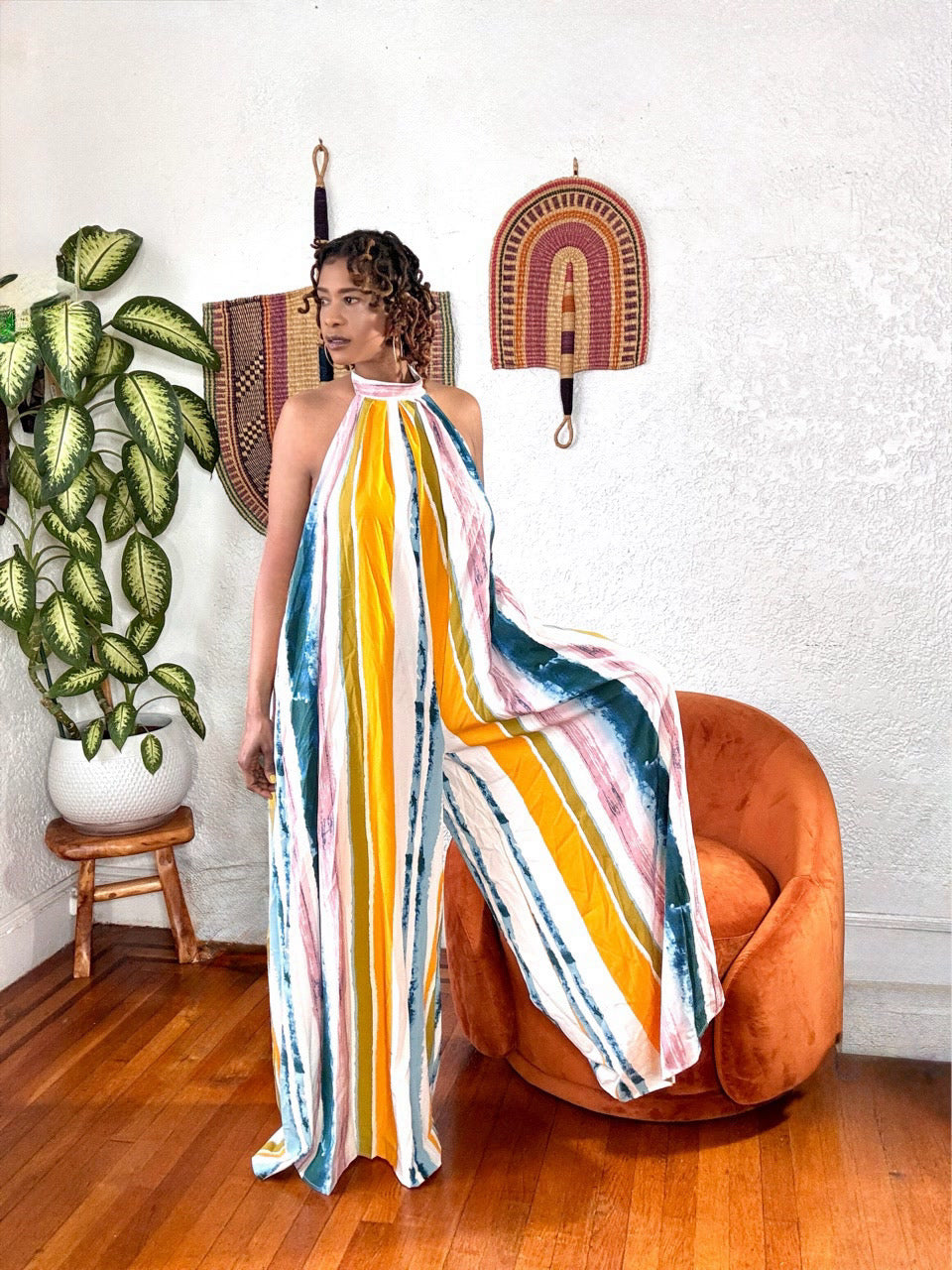 Model wearing the Sunset Drip Halter Jumpsuit from MonologueClosets — multicolor striped halter jumpsuit with wide legs and flowy fabric.